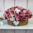 CESTO REDONDO M EM PALHA COM HORTÊNSIAS ENVELHECIDAS ROSADAS E CORAÇÃO 16AX32L/CM