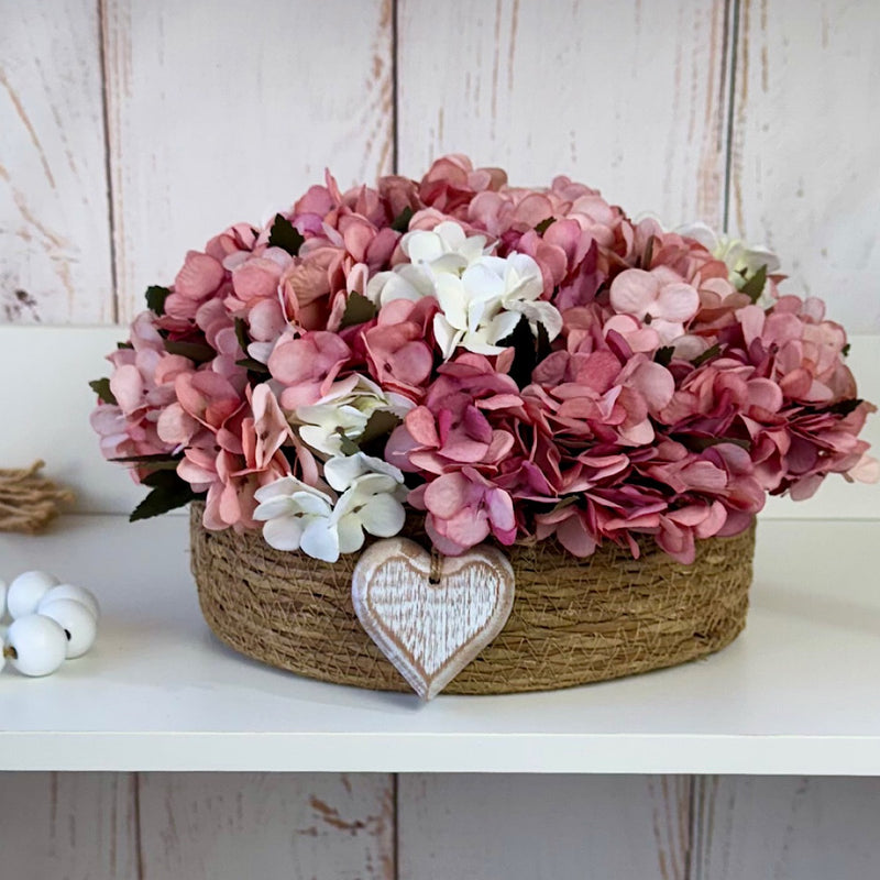 CESTO REDONDO M EM PALHA COM HORTÊNSIAS ENVELHECIDAS ROSADAS E CORAÇÃO 16AX32L/CM