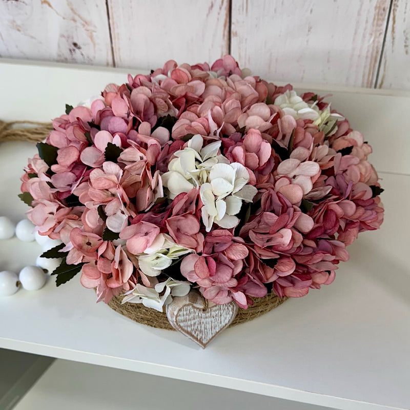 CESTO REDONDO M EM PALHA COM HORTÊNSIAS ENVELHECIDAS ROSADAS E CORAÇÃO 16AX32L/CM