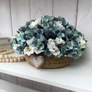 CESTO REDONDO M EM PALHA COM HORTÊNSIAS AZUIS ENVELHECIDAS E CORAÇÃO DE MADEIRA 16AX32L/CM